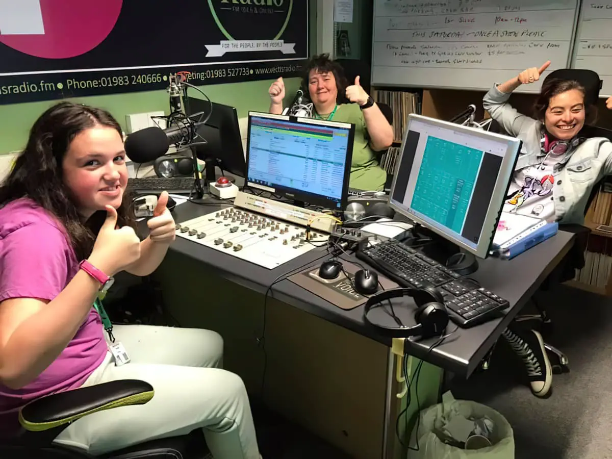 Three people giving thumbs up in the radio station's recording studio