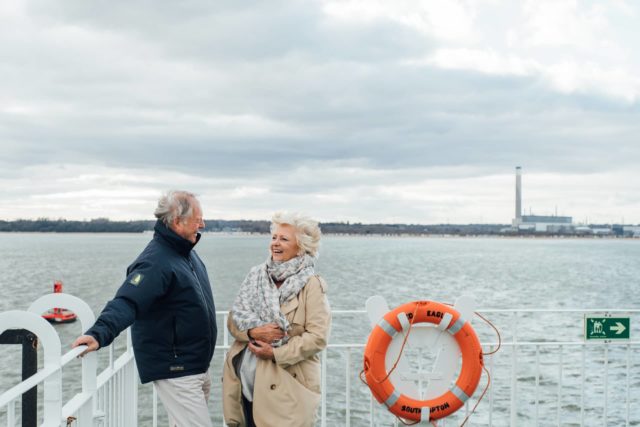 Mature man and woman on ferry open deck with Fawley Chimneys in background