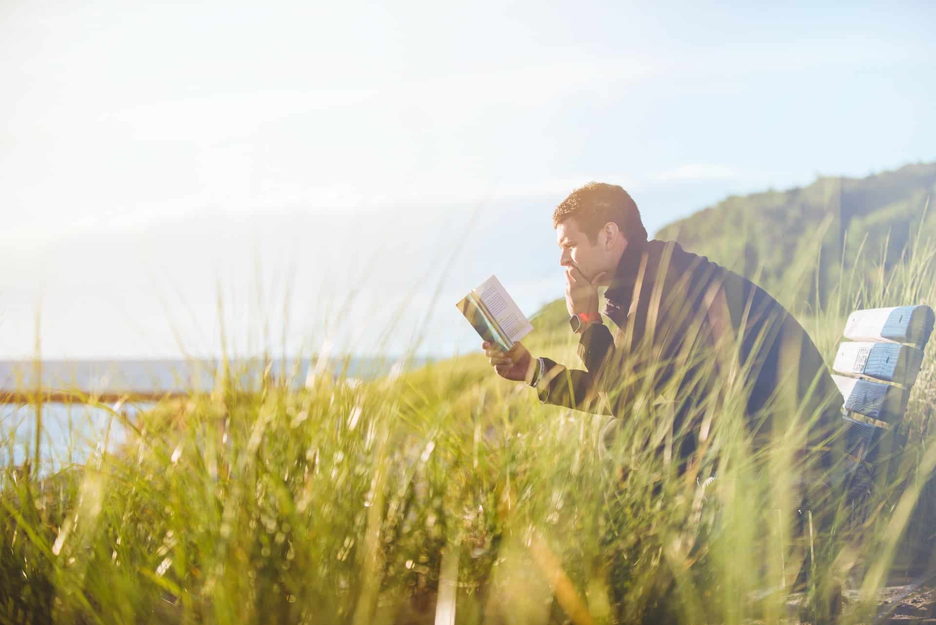 Man sat in chair in field reading a book by ben white
