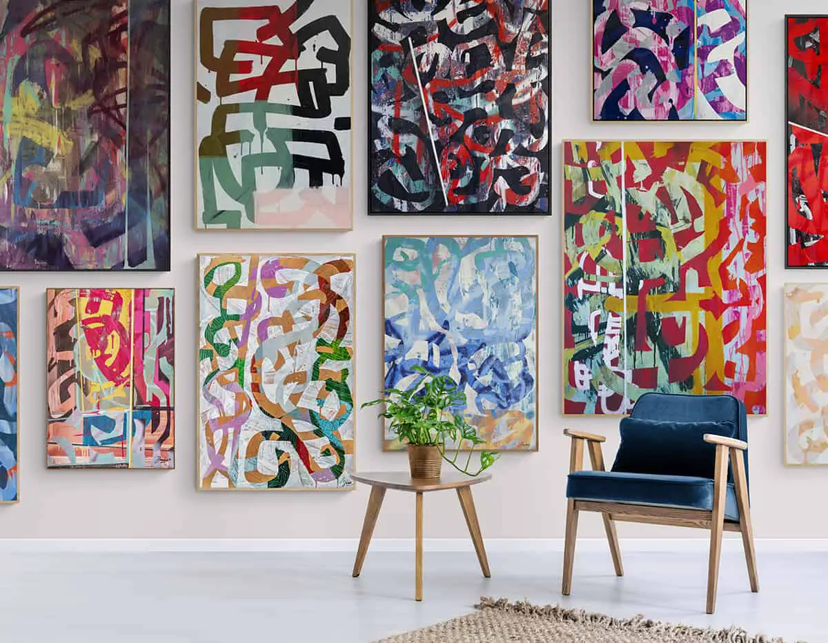 A number of paintings by Steve Miles hanging on a wall with a chair and side table in front of them