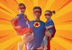 Father holding two daughters, all three of them dressed as superheroes