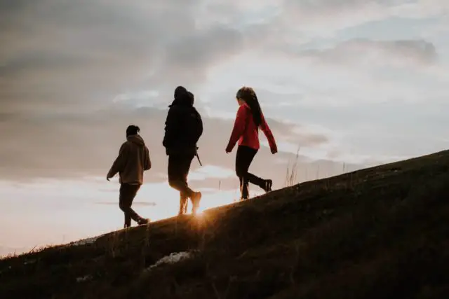 Three people walking down a hill with the sunset in the background