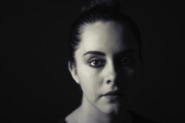 woman against dark background with tears on her cheeks - possible abuse or domestic violence