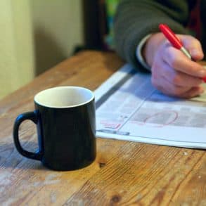 Person marking job ads in a paper, whilst sat at table with mug of tea