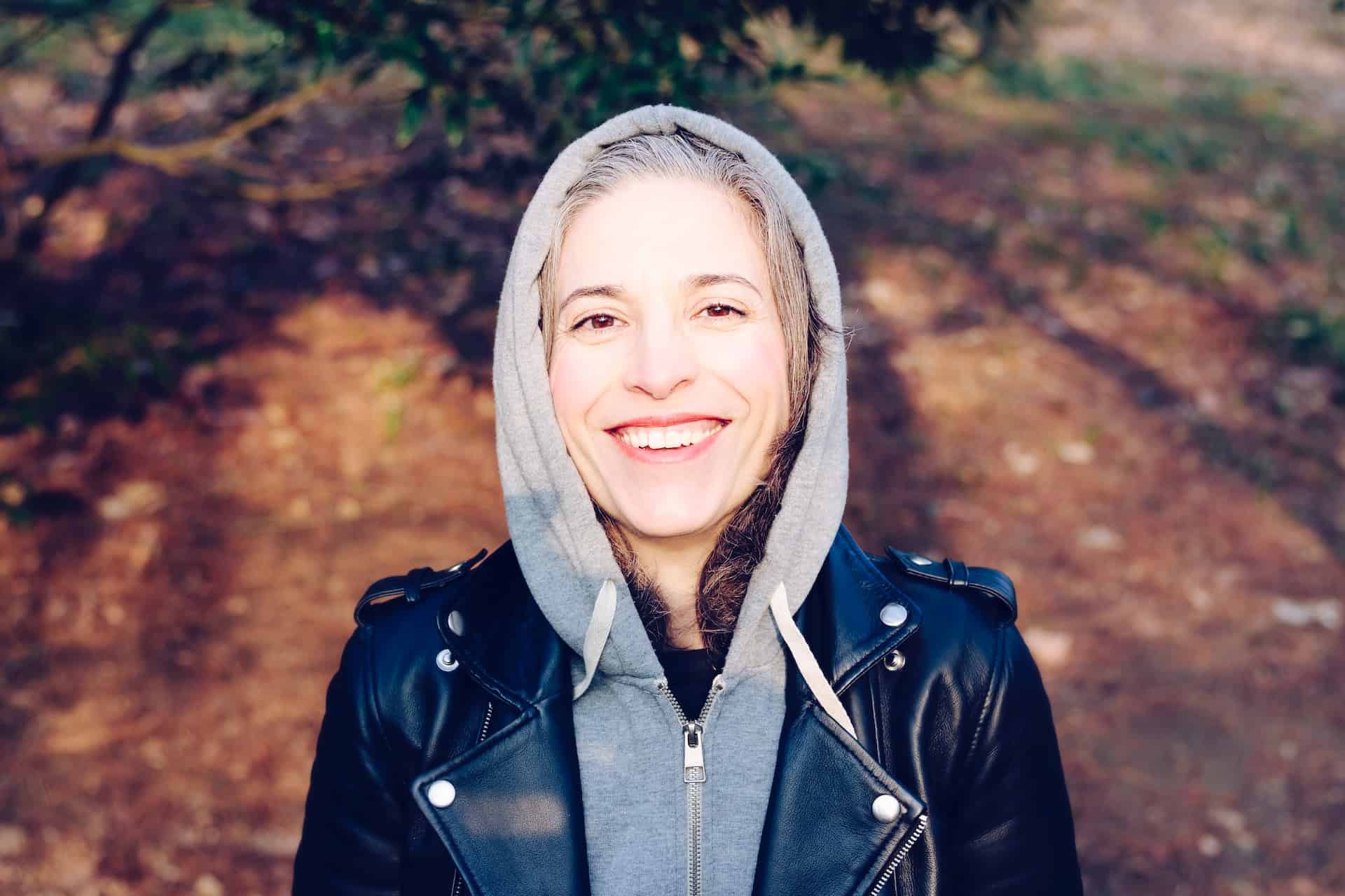 middle aged woman in hoodie in woods smiling to the camera
