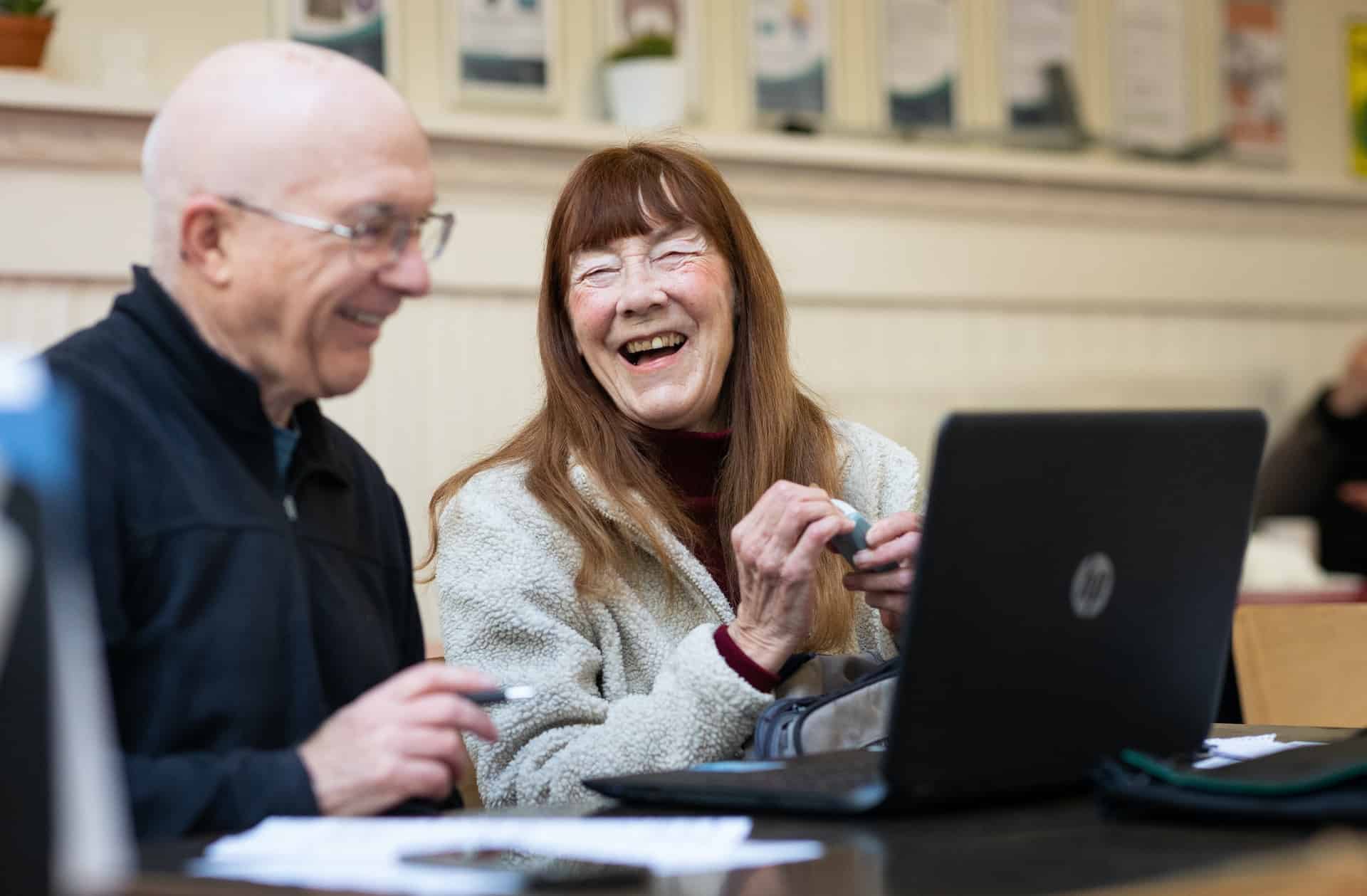 two older people sitting in front of laptops