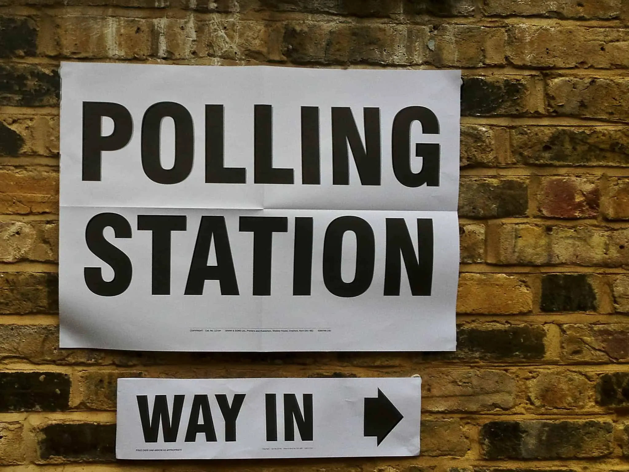Polling station sign taped to a brick wall