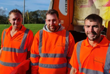 Three bin men at the back of the truck