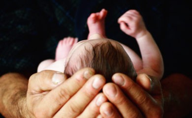 newborn baby cradled in man's hands