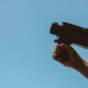 Person with camcorder in hand against a blue sky