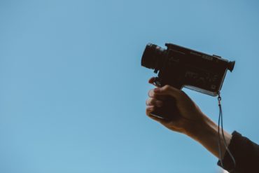 Person with camcorder in hand against a blue sky