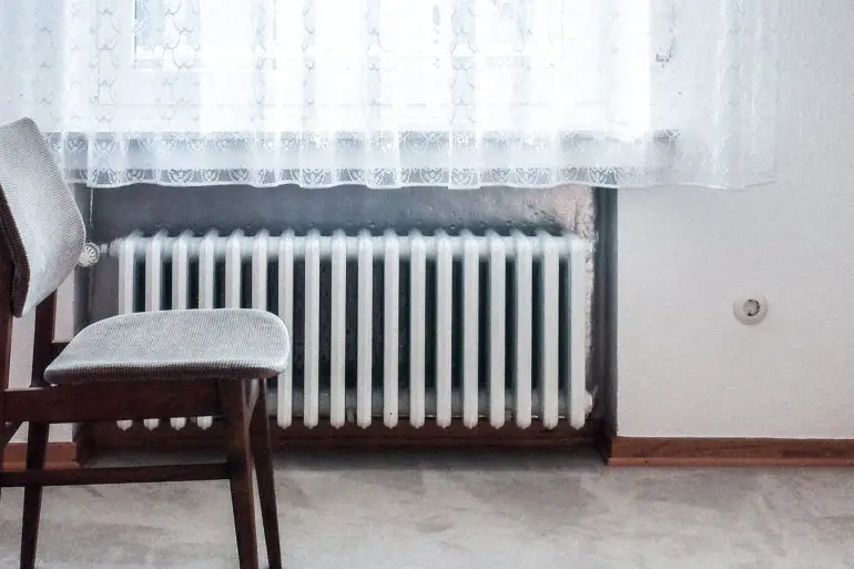 chair in front of window with radiator underneath it by dominik kuhn