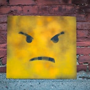 Angry face on yellow board leaning up against a brick wall