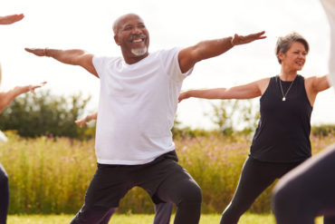 Female Teacher Leading Group Of Mature Men And Women In Yoga Class