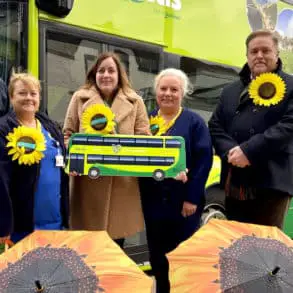 Southern Vectis staff with staff and CEO from Mountbatten Hospice standing by a bus with Sunflower umbrellas