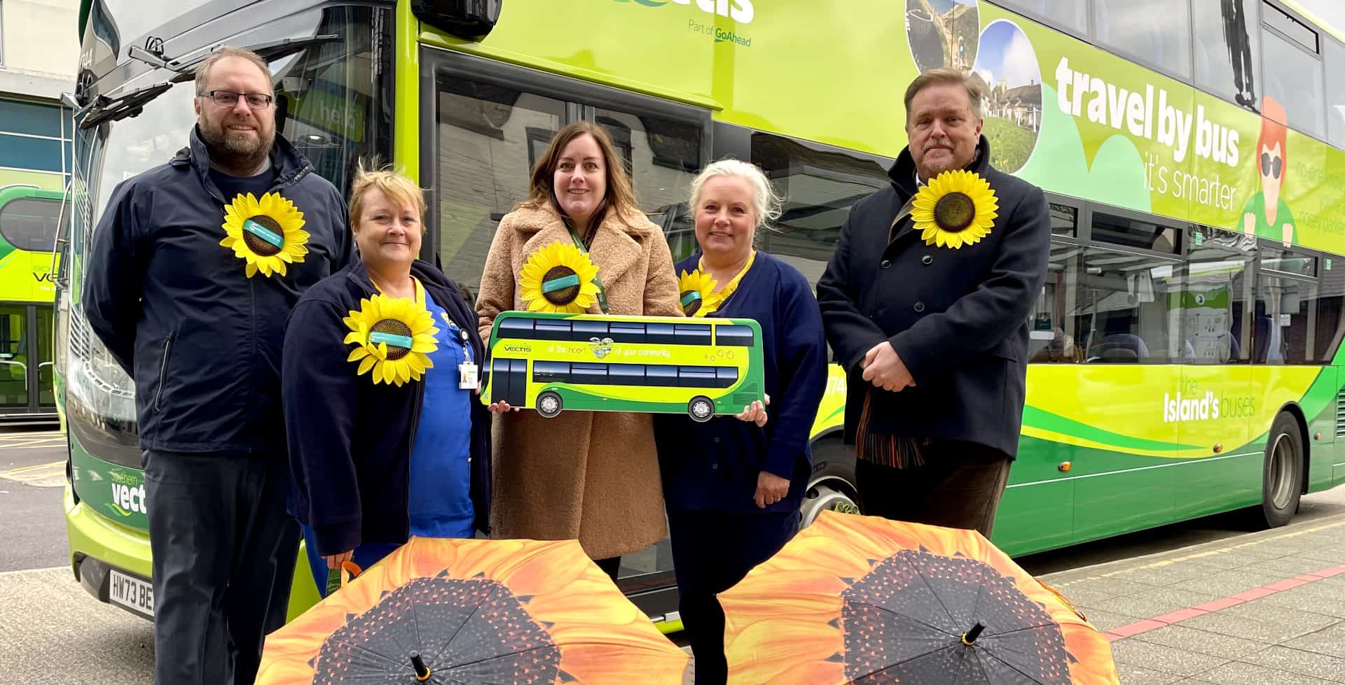 Southern Vectis staff with staff and CEO from Mountbatten Hospice standing by a bus with Sunflower umbrellas