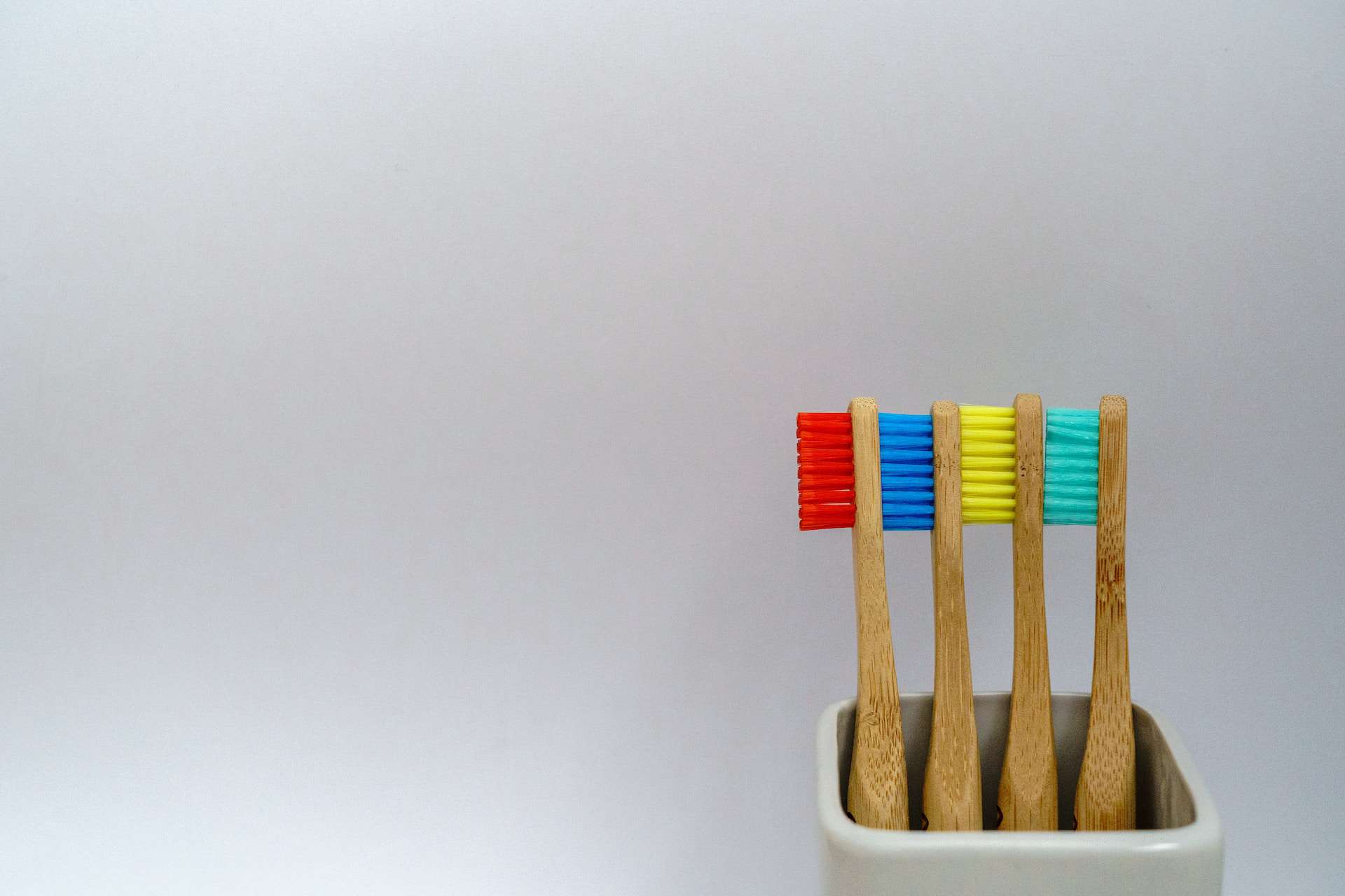 Toothbrushes in a cup with four different colours of brushes, red, blue, yellow and green