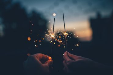 Two people holding burning sparklers in the garden