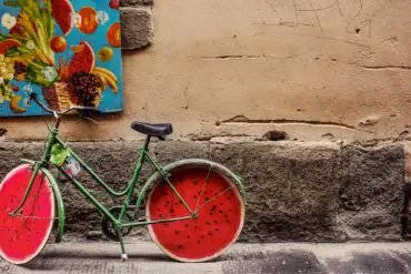 decorated bicyle next to brick wall with painting hanging on it