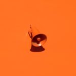 orange background with loud speaker attached to wall by oleg laptev