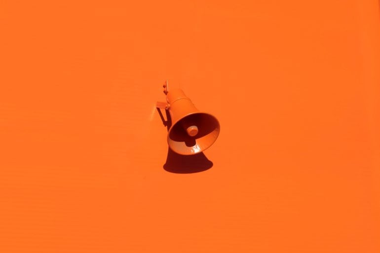 orange background with loud speaker attached to wall by oleg laptev