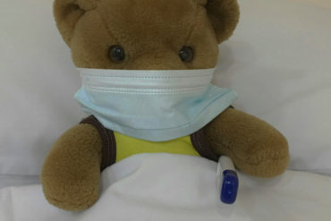 teddy in bed with face mask on and thermometer under arm