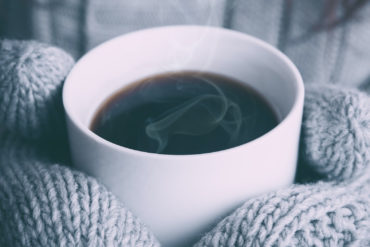woman wearing mittens whilst holding a mug of hot coffee