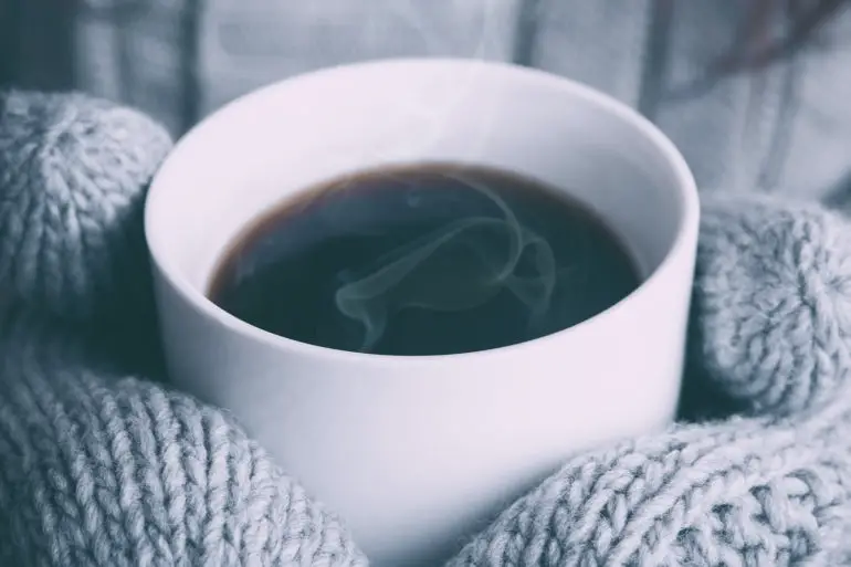 woman wearing mittens whilst holding a mug of hot coffee