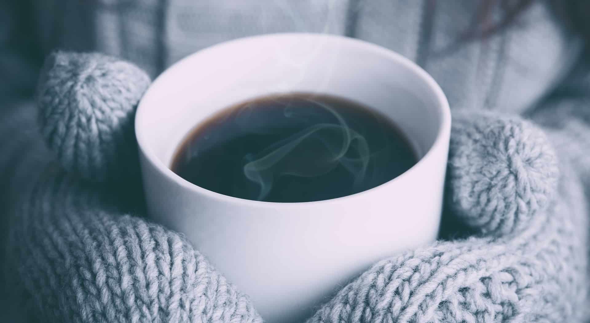 woman wearing mittens whilst holding a mug of hot coffee