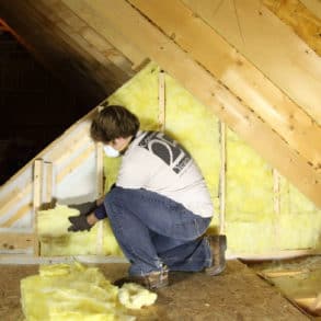 Man with mask on putting insulation into an attic