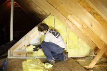 Man with mask on putting insulation into an attic