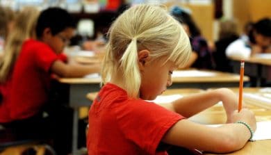 Girl sat in class writing with pencil and paper