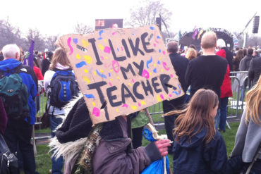 'I like my teacher' banner being held by young person in crowd at rally