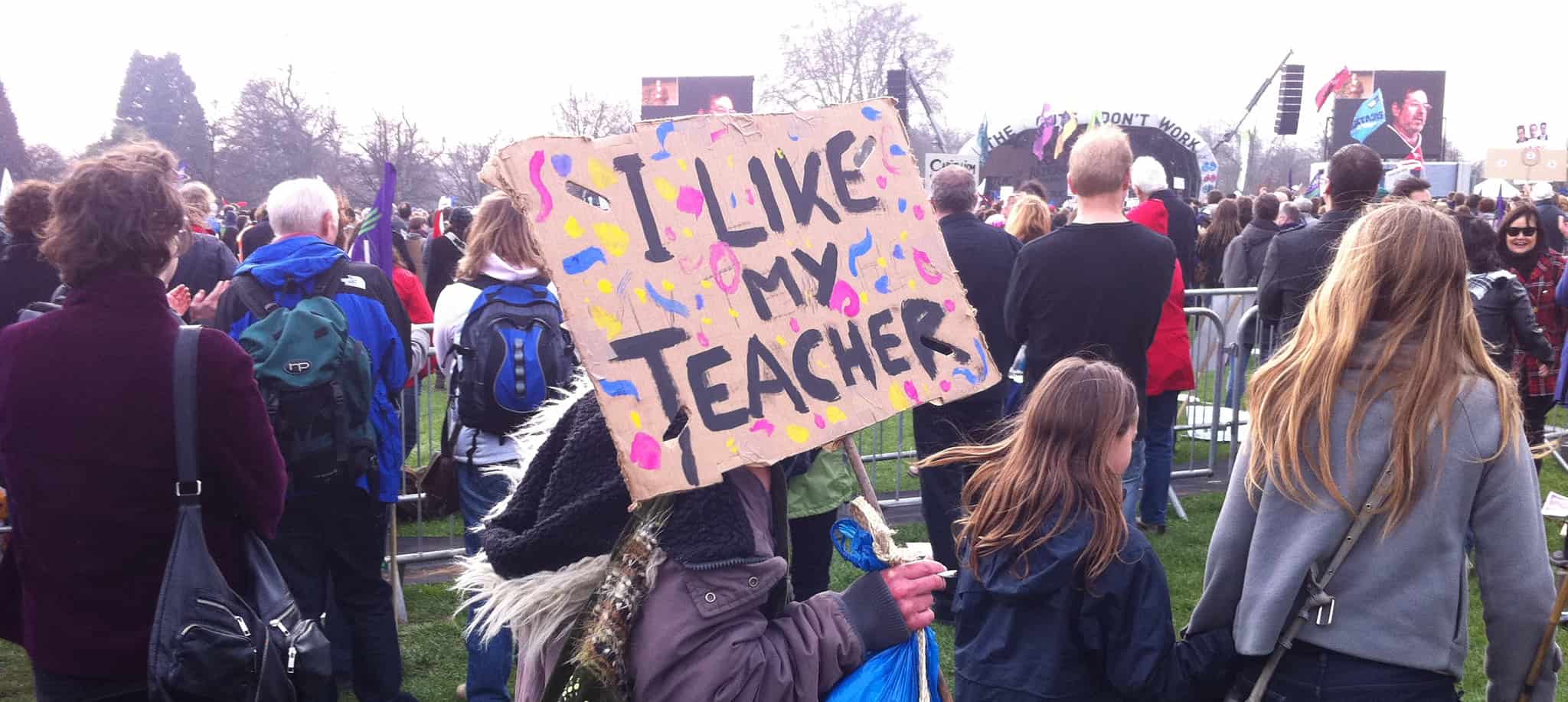 'I like my teacher' banner being held by young person in crowd at rally