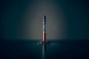 Smoking cigarette balanced on filter with ash around it