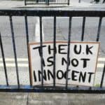 handmade sign attached to railings in London that reads 'the UK is not innocent'