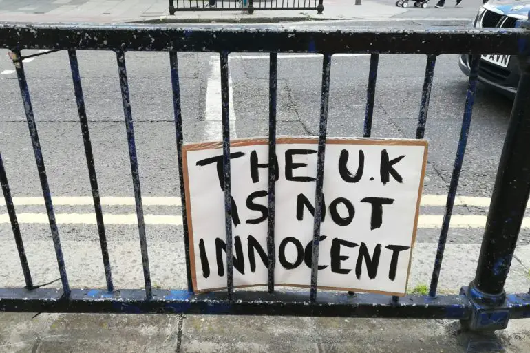 handmade sign attached to railings in London that reads 'the UK is not innocent'