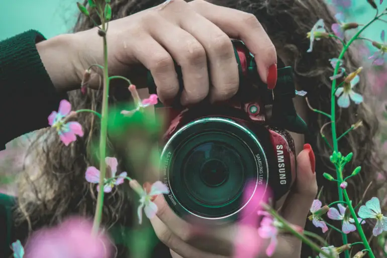 Woman using a camera through flowers to take photo