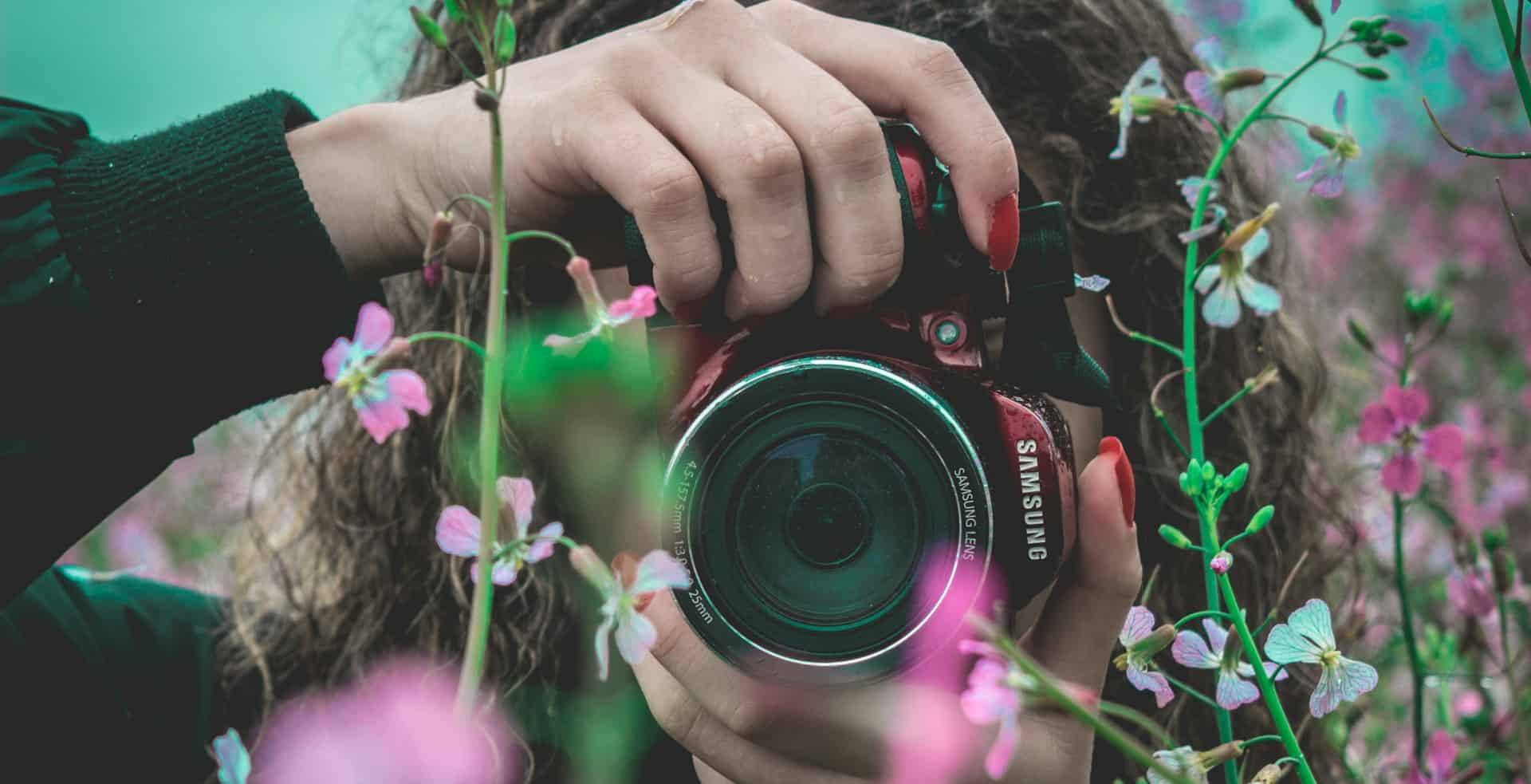Woman using a camera through flowers to take photo