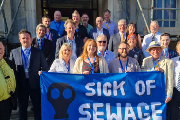 Councillors outside county hall holding a 'sick of sewage' banner