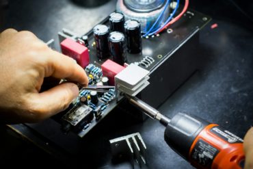 person repairing a circuit board with a drill