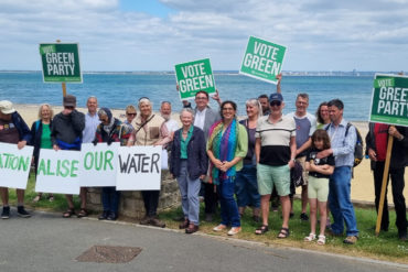 Green Party members with candidates and Baroness Jenny Jones on seafront holding banners