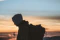silhouette of man with large rucksack on his back with sunset in the background by dimi katsavaris