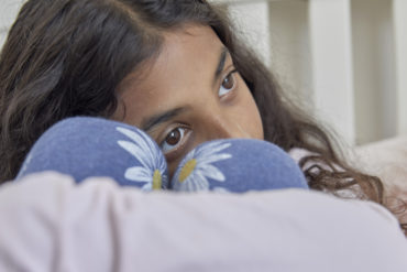 Young female teenager sat with her knees bent up in front of her, hugging them