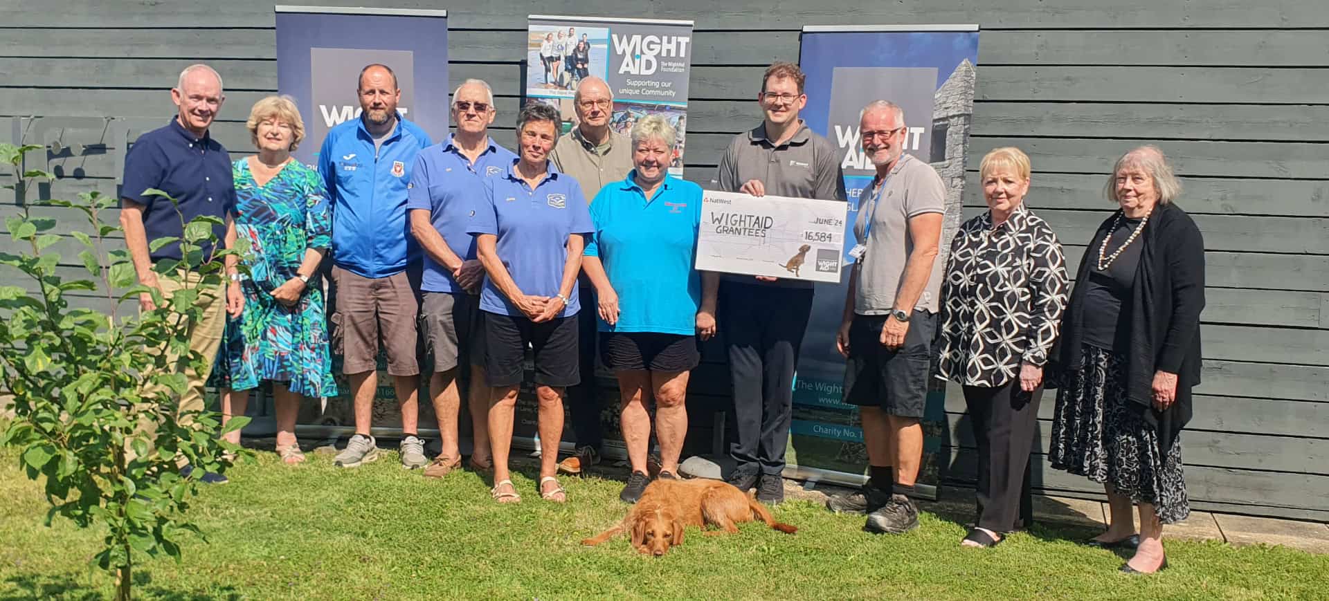 People standing outside a building with a giant cheque from Wight Aid