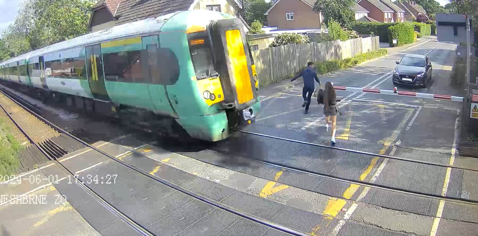 Two people rushing across the level crossing narrowly missed by the oncoming train