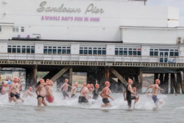 People taking part in the Pier to pier swim by running into the water by Sandown pier