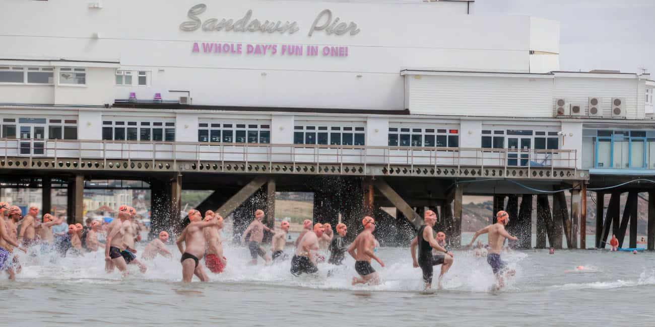 People taking part in the Pier to pier swim by running into the water by Sandown pier