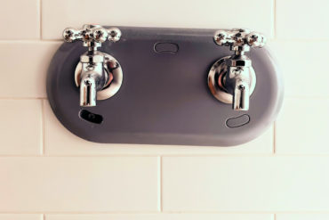 a pair of chrome taps set into a white tiled wall
