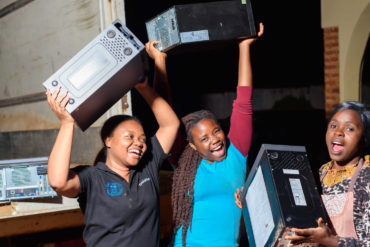 children in africa holding up laptops and smiling